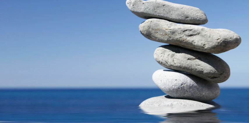 <p>Stack of pebbles in shallow water with blue sky background</p>
